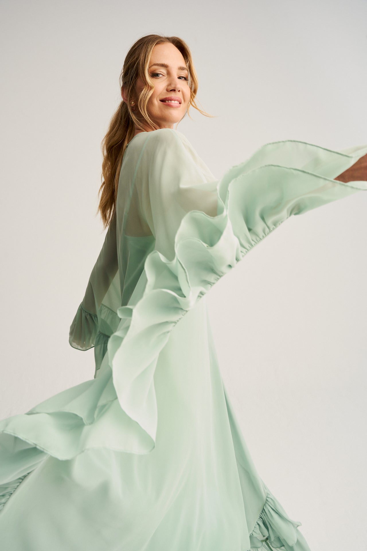 Vestido largo de invitada en tono menta con vuelo, diseño exclusivo con capa de gasa ligera y detalles en volantes, perfecto para eventos elegantes.